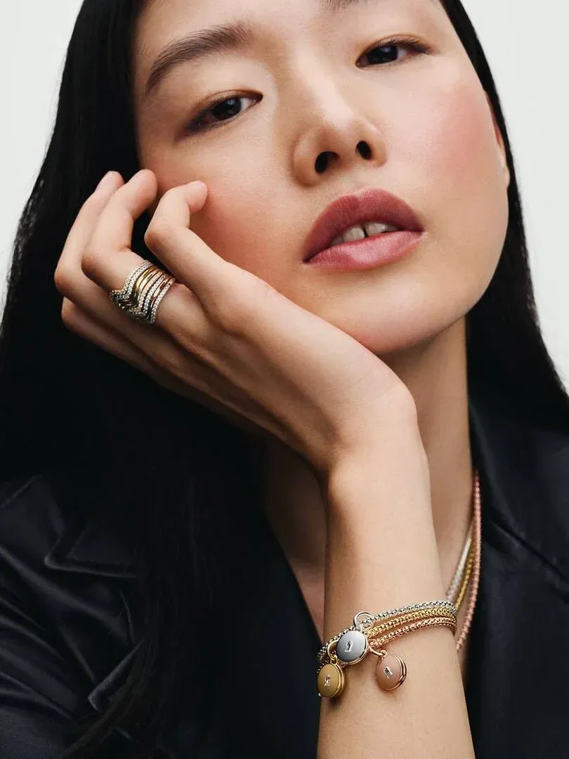 Primer plano de modelo con anillos dorados en los dedos y pulseras con colgantes en la muñeca.