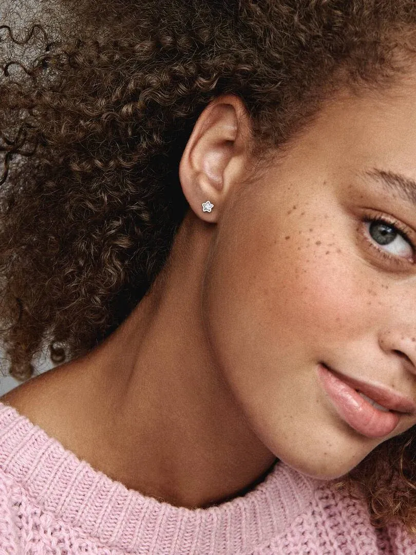 Gros plan latéral d'une boucle d'oreille étoile en argent sur le lobe de l'oreille, modèle aux cheveux bouclés.