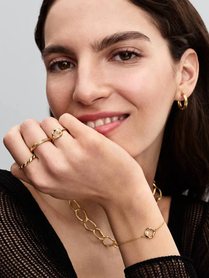 Primer plano de modelo sonriendo con anillo y pulsera dorada, toma lateral enfocada en la mano y rostro.