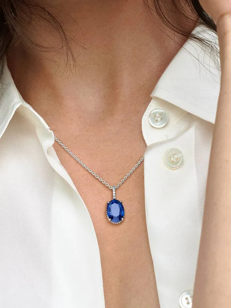 Primer plano del colgante azul sobre una camisa blanca, toma frontal en el cuello de una modelo.