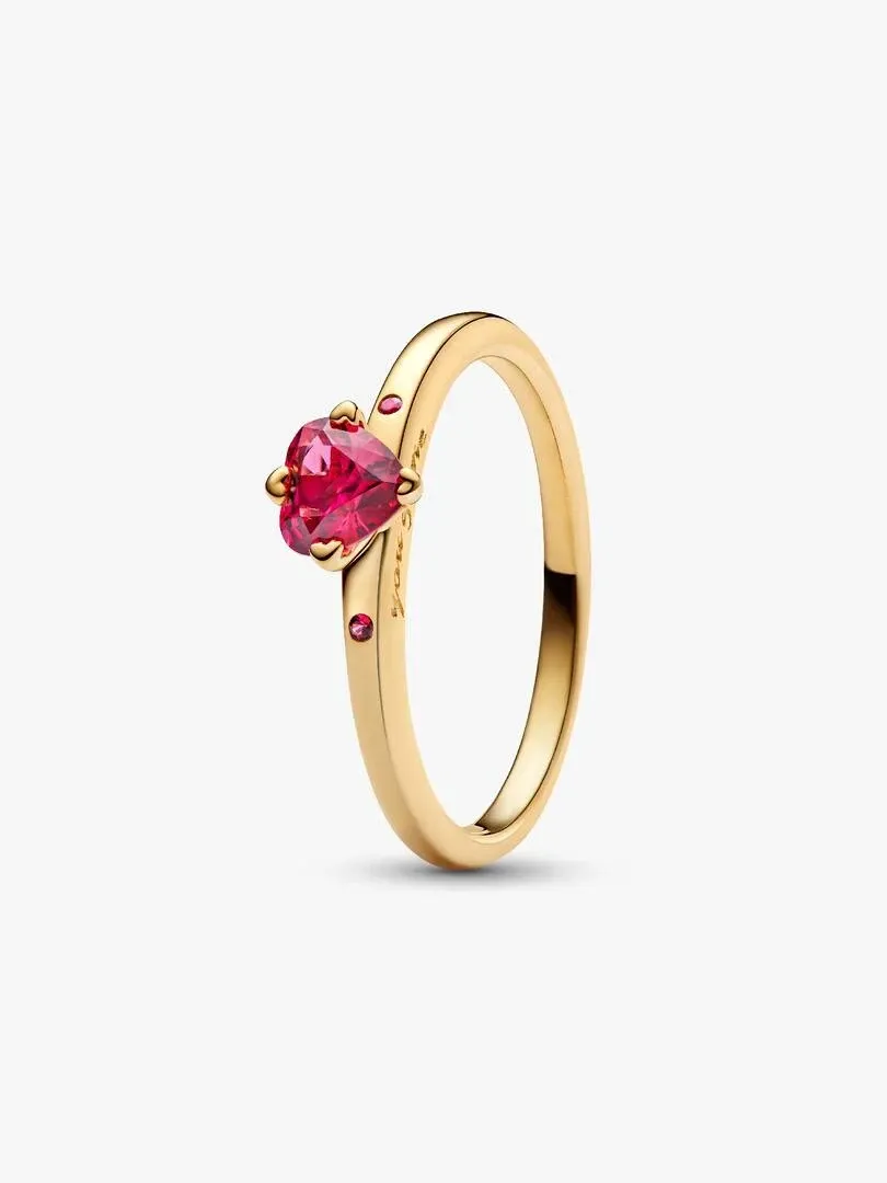 Anillo con cristal rojo en forma de corazón, vista lateral en ángulo sobre fondo blanco.