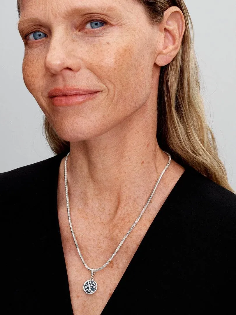 Gros plan du collier avec pendentif arbre porté sur le cou d'un modèle, fond neutre clair.