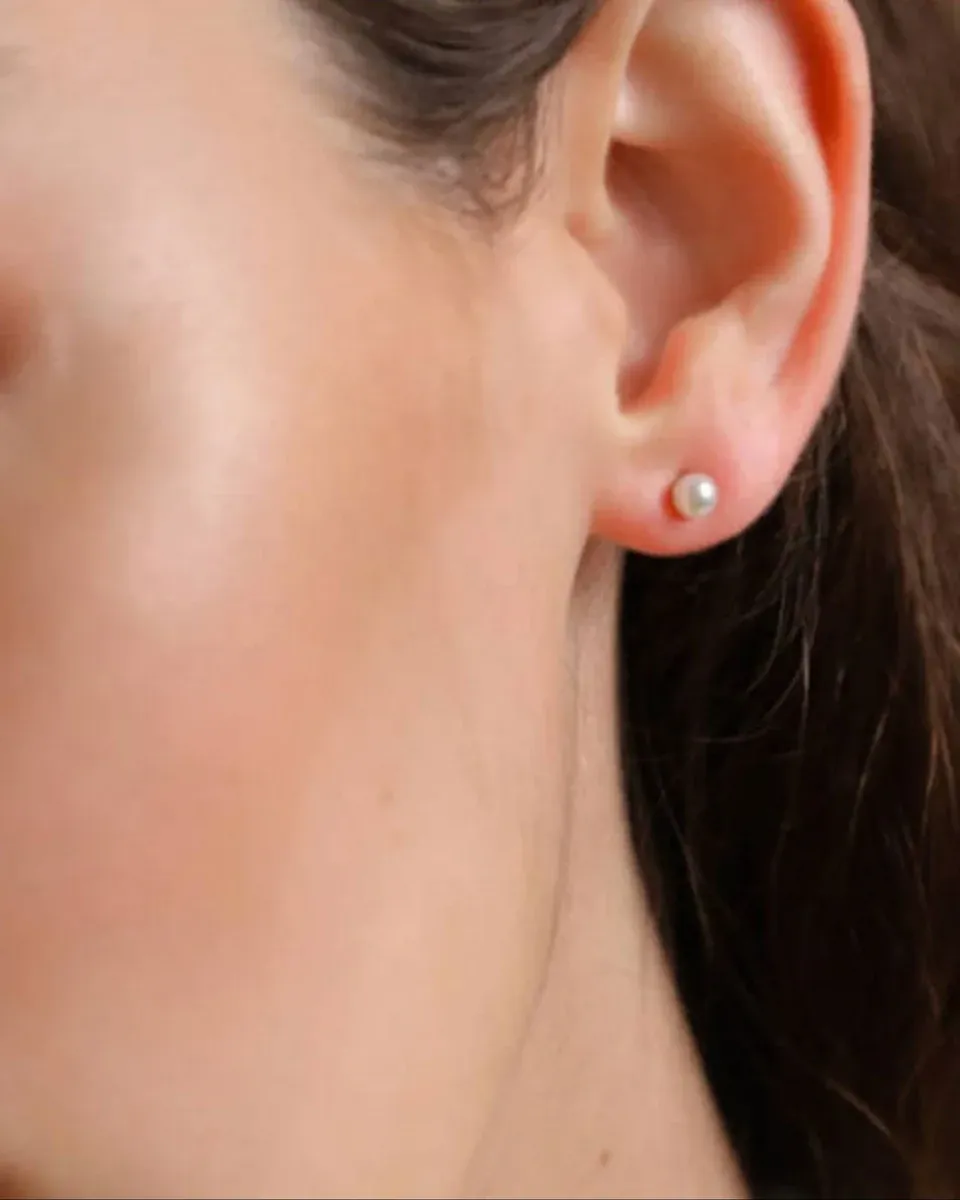 Close-up side view of a white pearl stud earring worn on the earlobe.