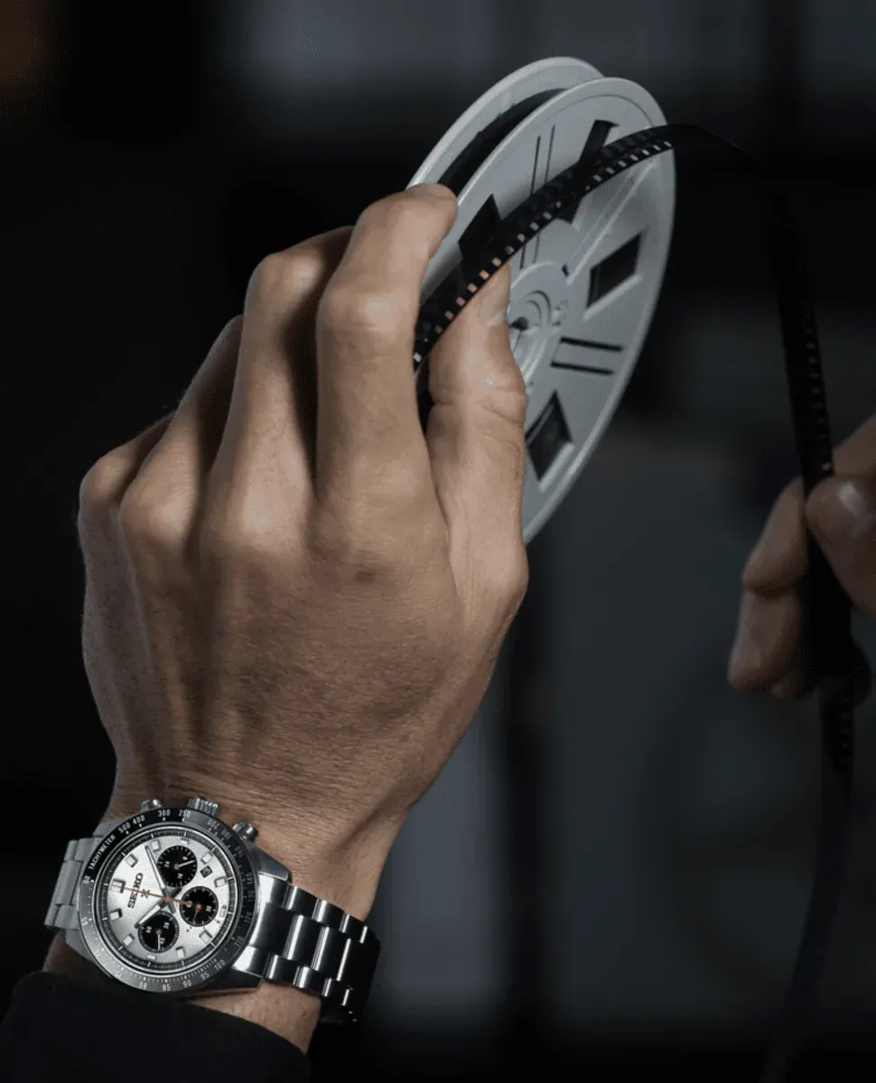 Reloj puesto en muñeca masculina mientras sostiene un carrete de película, fondo oscuro desenfocado
