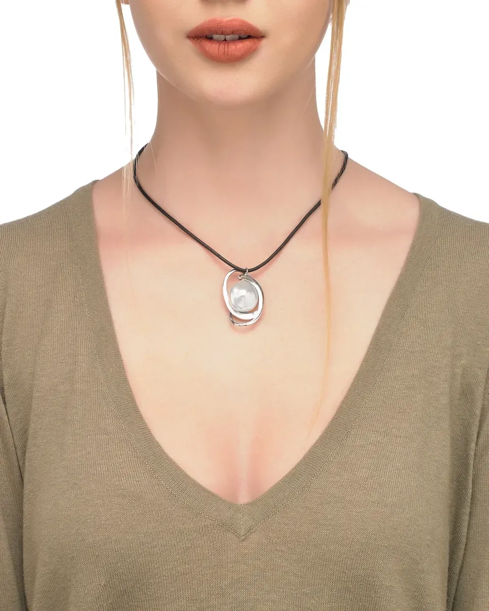 Close-up of the pearl pendant on a black cord, worn on a model's neck with a beige sweater.