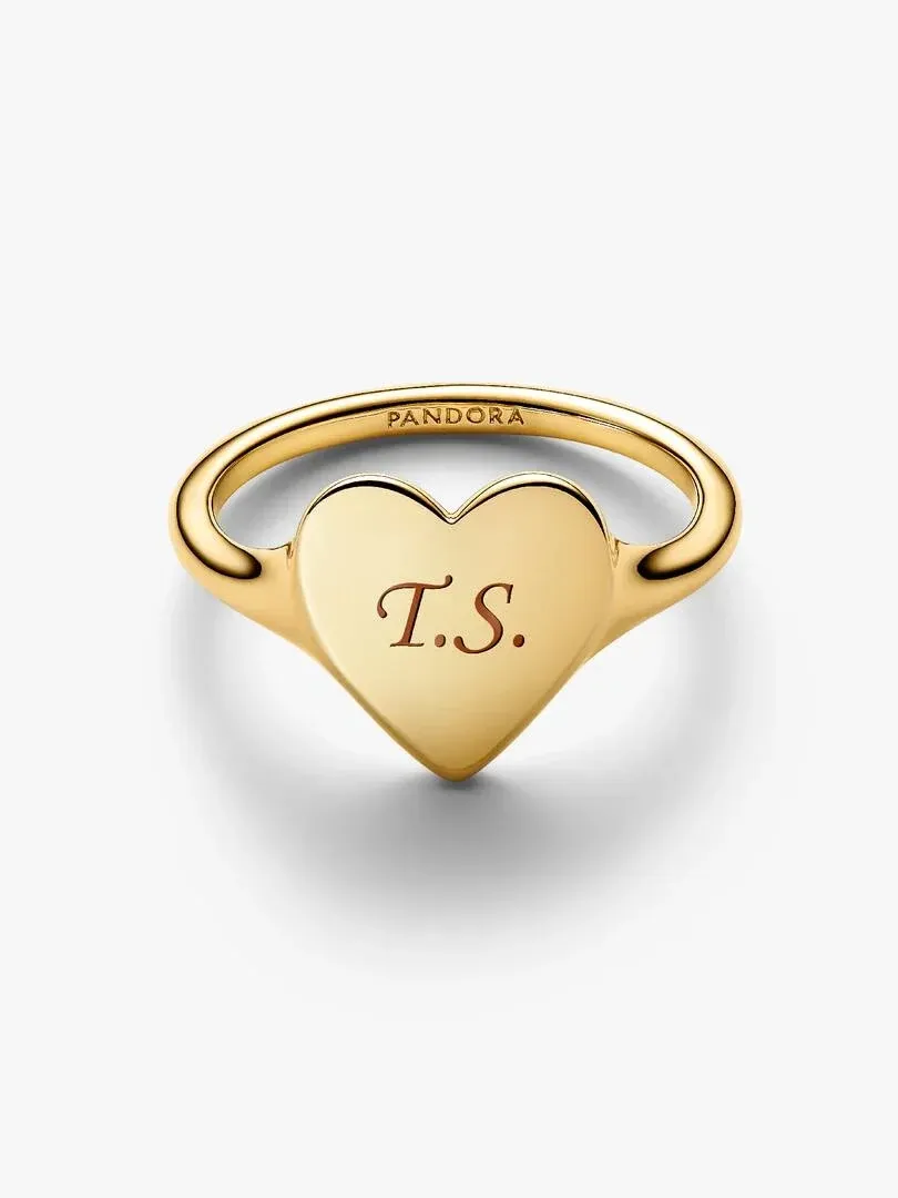 Anillo de corazón dorado con grabado 'T.S.', vista frontal en ángulo, fondo blanco neutro.
