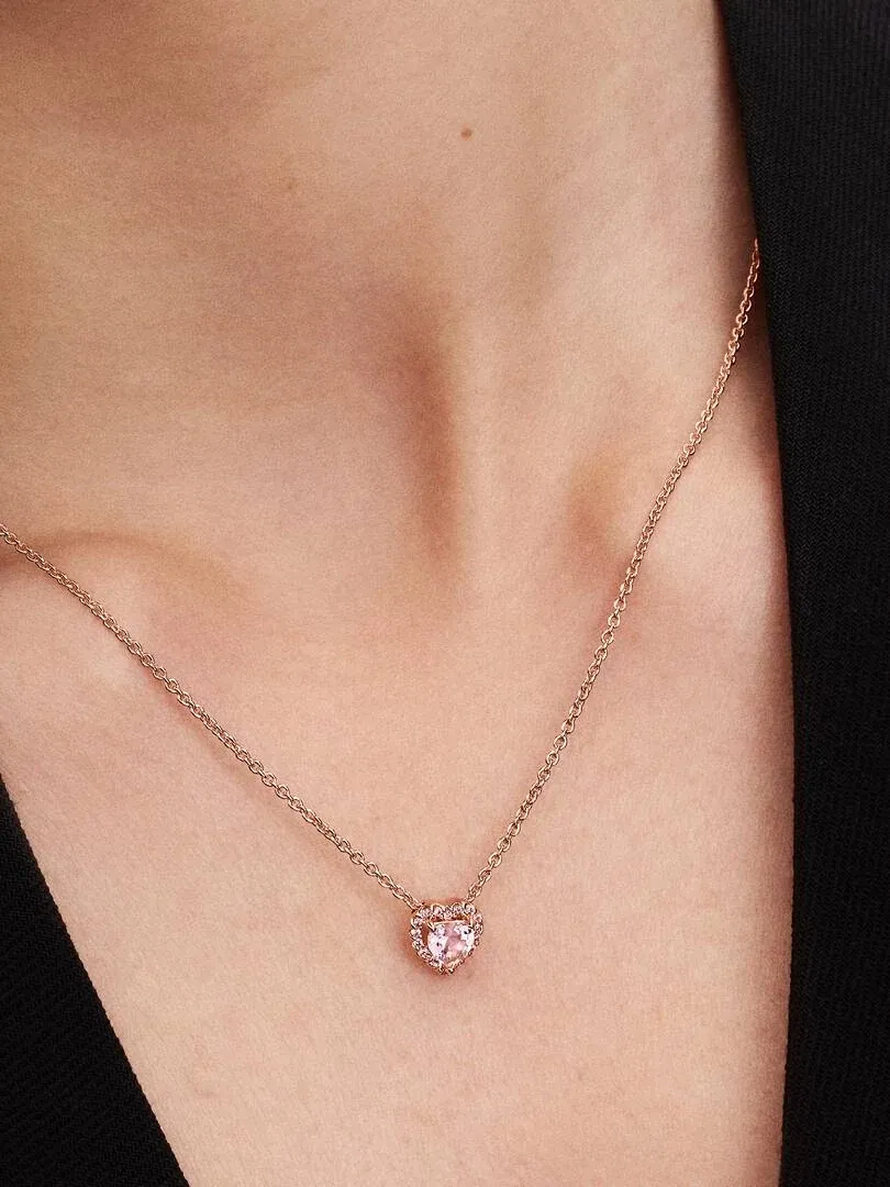 Gros plan du collier avec pendentif cœur rose porté sur le cou d'un mannequin, fond sombre.