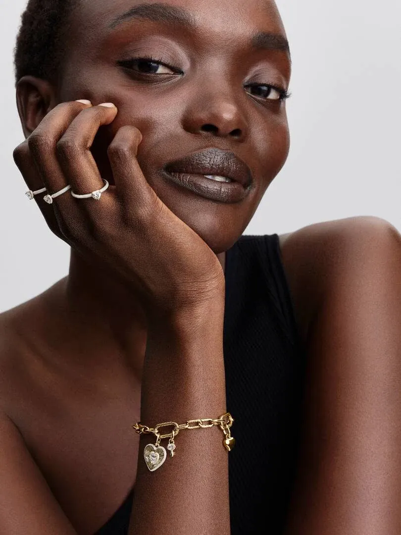 Gros plan du poignet avec bracelet chaîne doré et pendentif cœur, modèle appuyant son visage sur sa main.