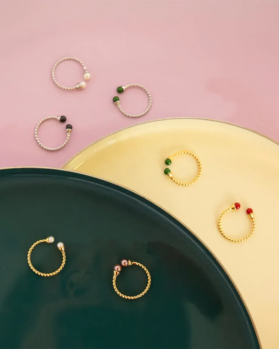 Variedad de anillos Twist con perlas dispuestos sobre platos circulares en tonos crema y verde oscuro.