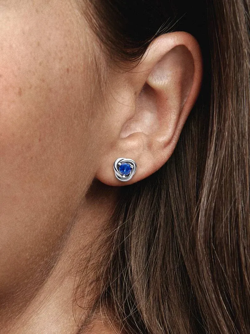 Primer plano lateral de pendiente de botón con cristal azul en el lóbulo de la oreja.