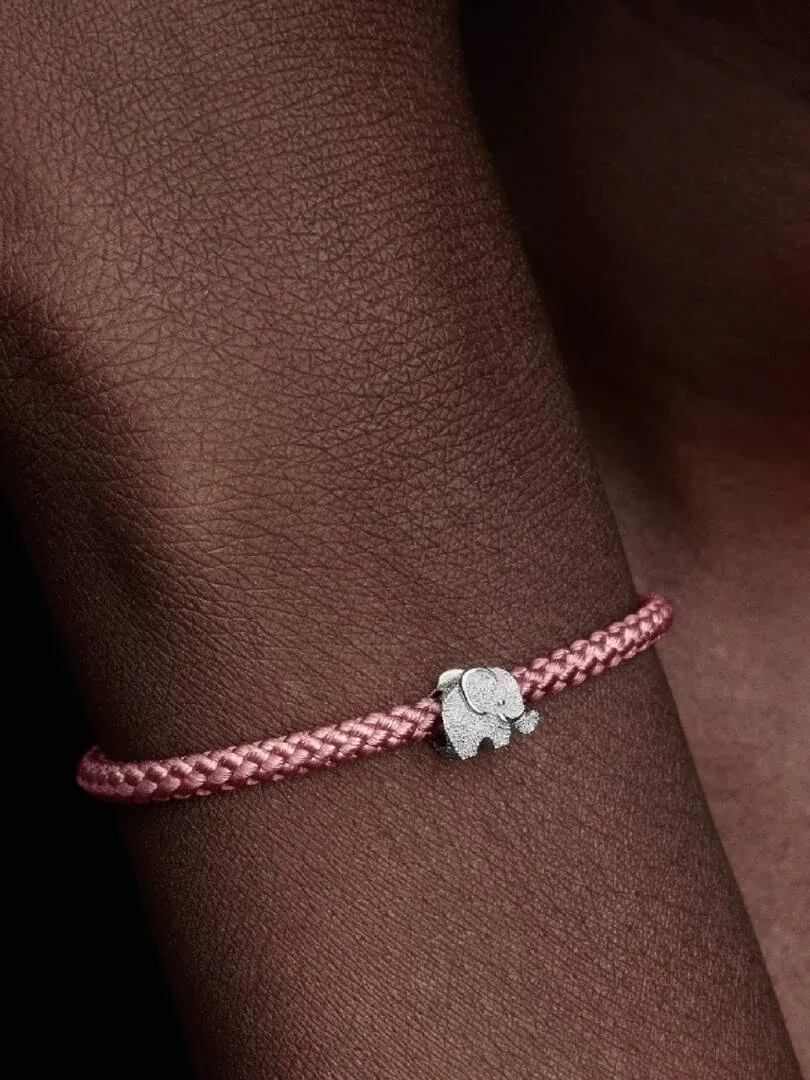 Primer plano del charm de elefante en plata sobre una pulsera trenzada rosa, puesto en la muñeca.