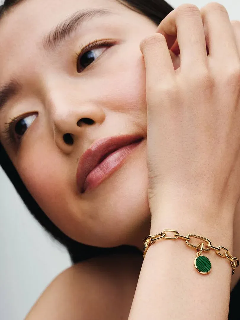 Gros plan du bracelet avec charm vert au poignet, vue de profil avec modèle flou en arrière-plan.