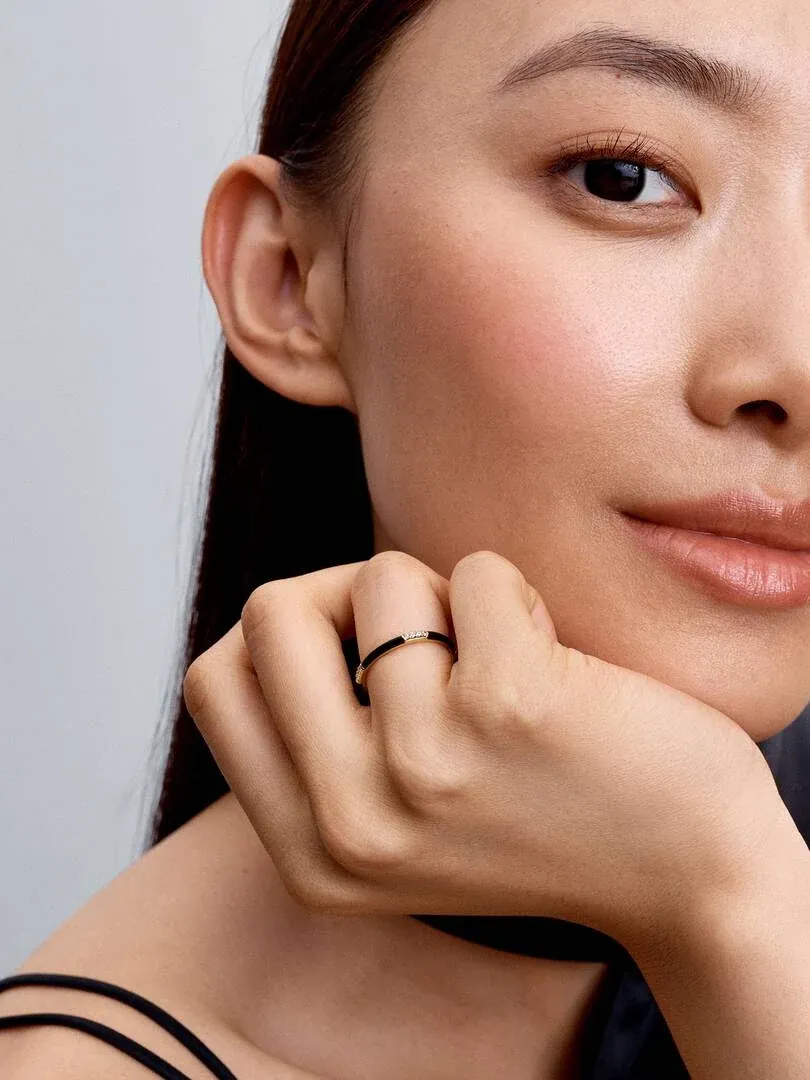 Primer plano de anillo con esmalte negro y circonitas en dedo, modelo apoyando la barbilla sobre la mano.