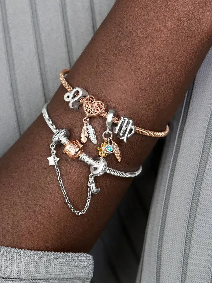Close-up of two charm bracelets on a wrist, side view against a grey knit fabric background.