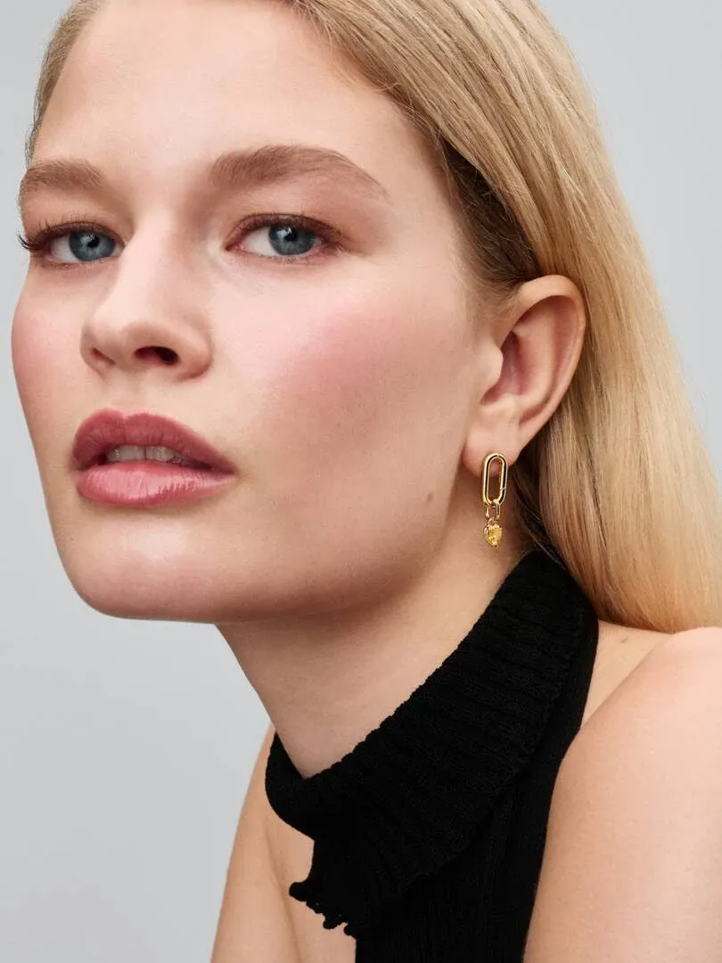 Close-up side view of a gold drop earring with yellow cubic zirconia worn on a model's ear.