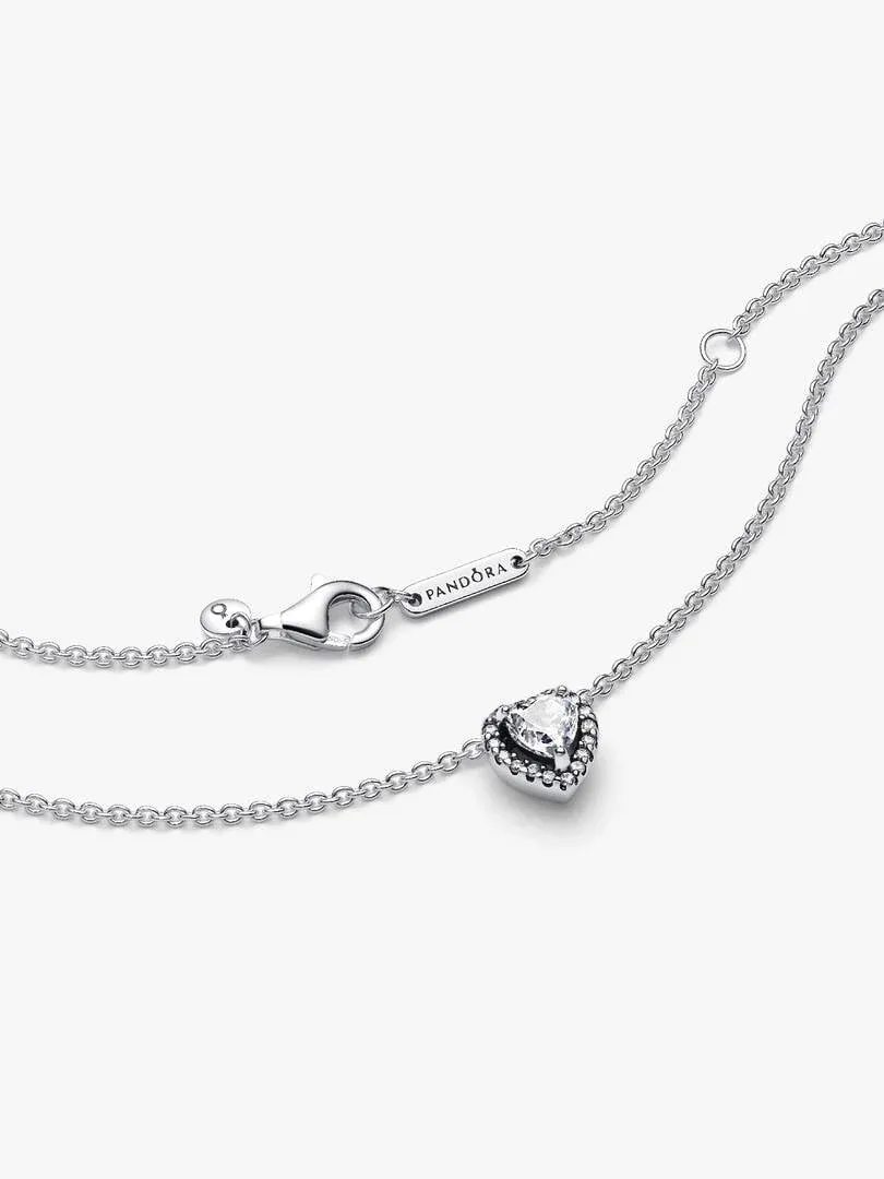 Primer plano del colgante de corazón y el cierre con logotipo, sobre fondo blanco.