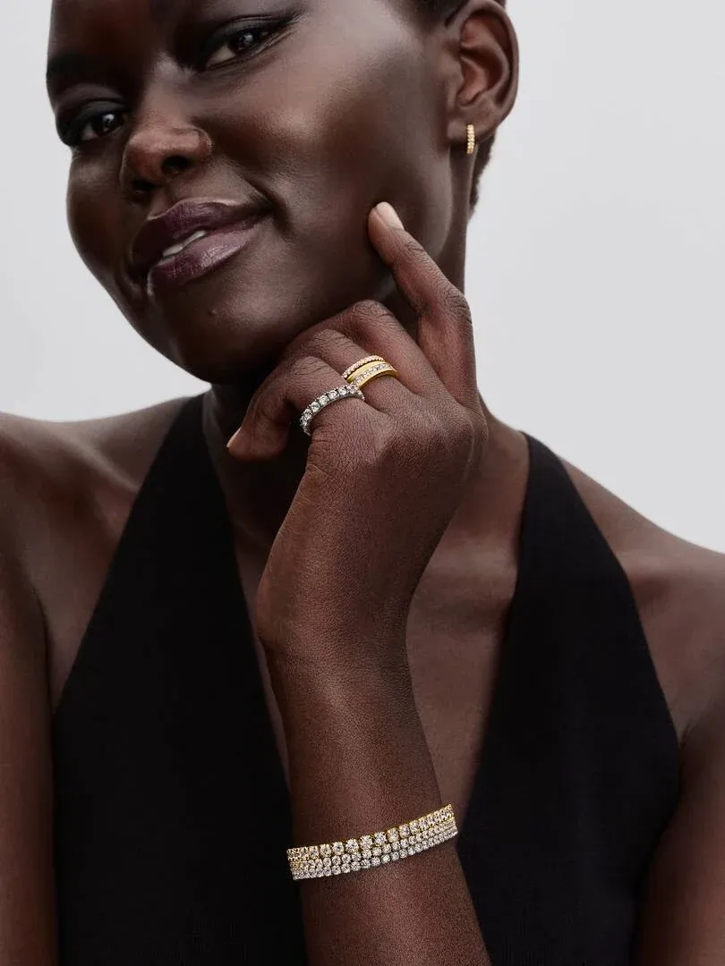 Primer plano de pulsera y anillos en una modelo, toma lateral con fondo neutro desenfocado.