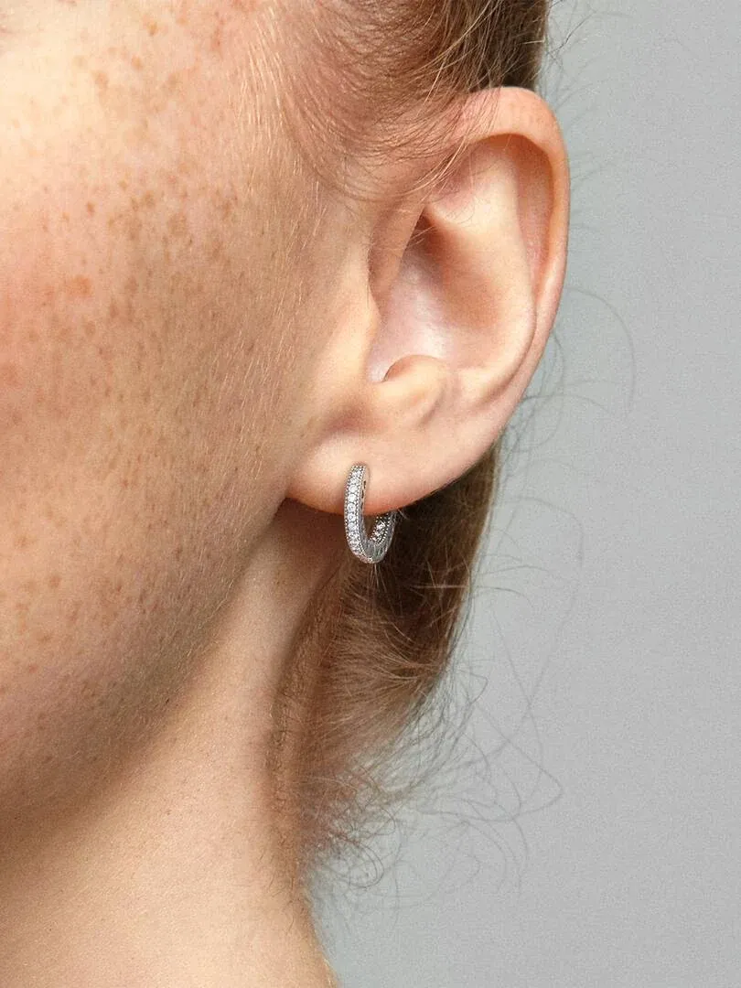 Side close-up of a pavé hoop earring worn on an earlobe, neutral gray background.