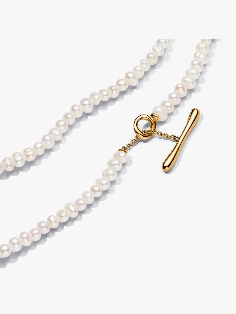 Primer plano del cierre de barra en T dorado y las perlas blancas sobre fondo blanco.