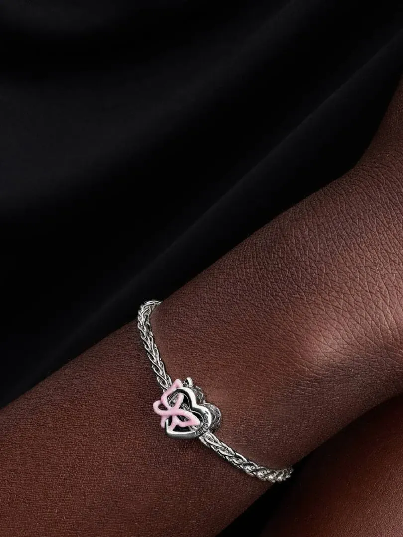 Primer plano del charm en una pulsera de plata sobre la muñeca, toma lateral con fondo oscuro desenfocado.