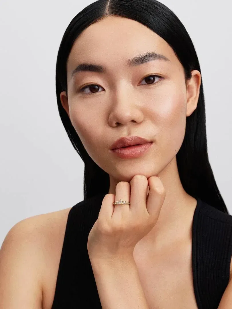 Primer plano de modelo con el anillo en el dedo anular, mano apoyada en la barbilla sobre fondo neutro.