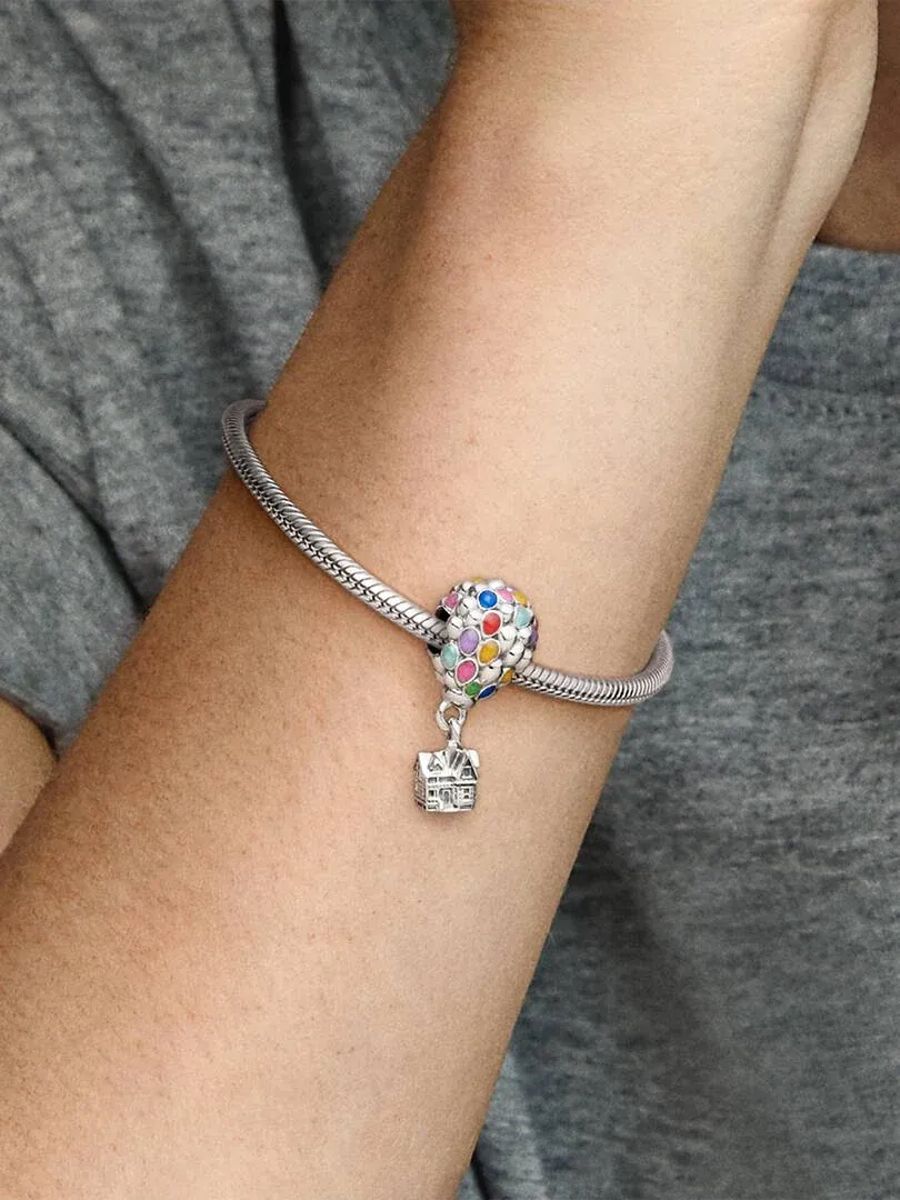 Primer plano de un charm de Disney Up en una pulsera de plata, puesto en la muñeca con fondo gris.
