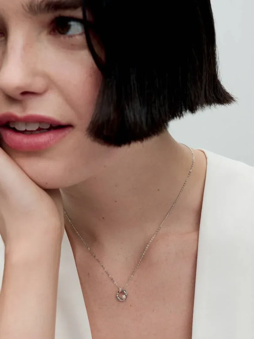 Primer plano del collar con perla y pavé sobre el cuello de una modelo, toma frontal con fondo neutro.