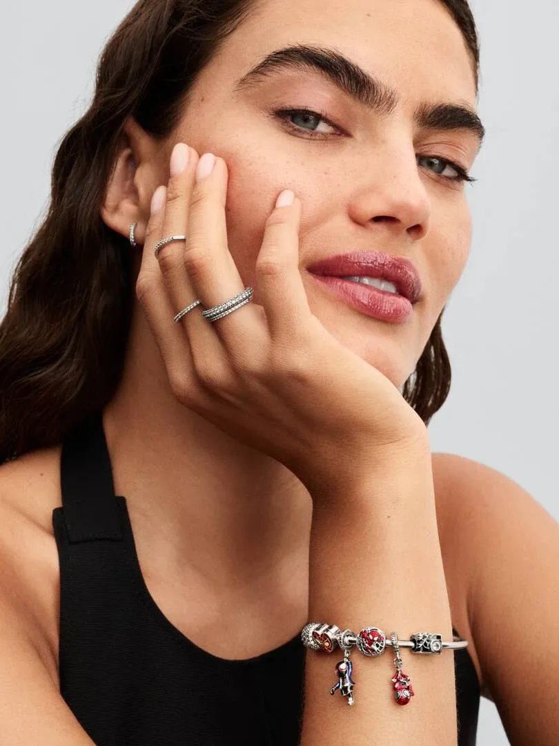 Gros plan d'un modèle portant un bracelet à charms et des bagues en argent, vue de profil.