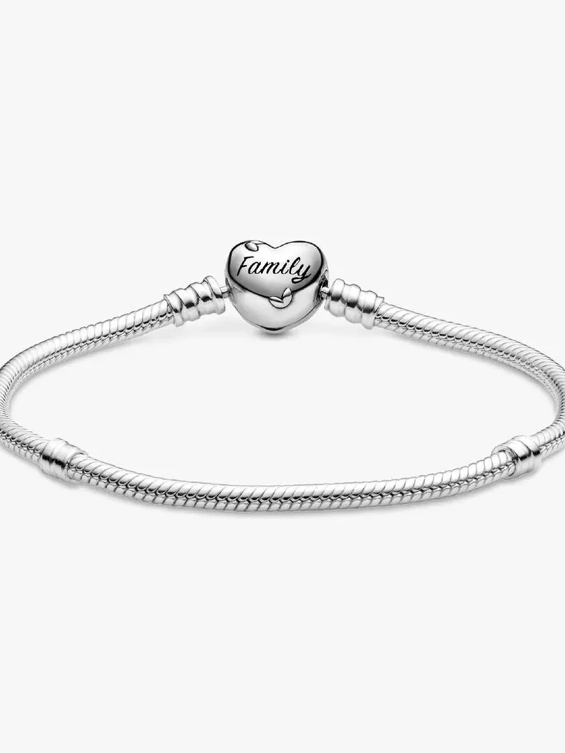 Primer plano del cierre de corazón con la inscripción 'Family', sobre pulsera de cadena de serpiente, fondo blanco.