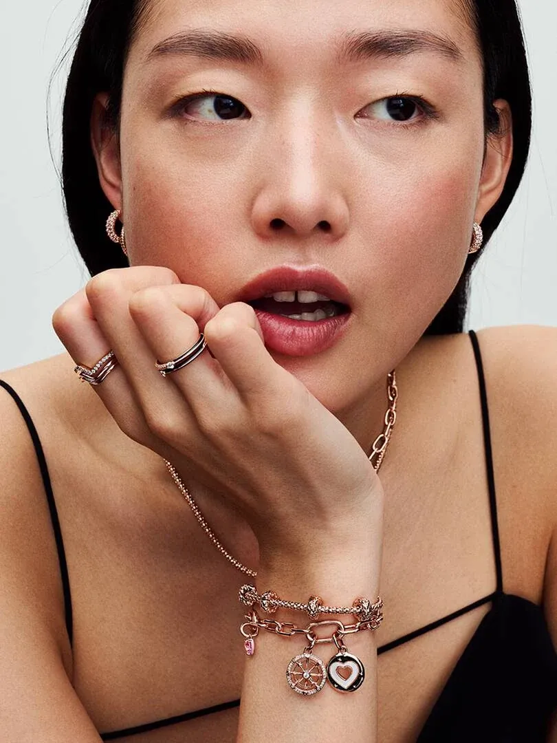 Primer plano de modelo luciendo pulsera con charms y anillos, toma lateral enfocada en la mano y rostro.