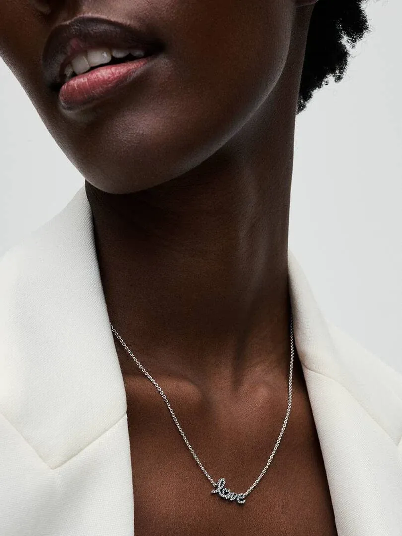 Primer plano del collar con colgante de palabra sobre el cuello de una modelo, fondo neutro claro.