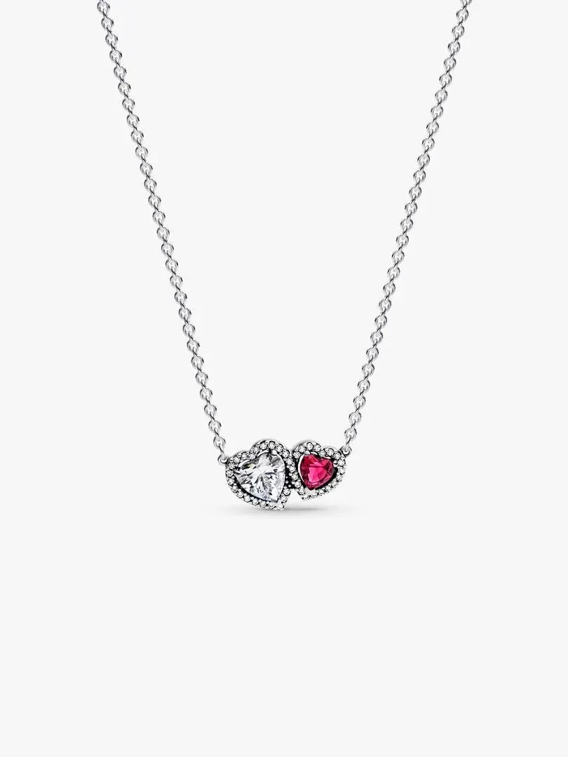 Collier en argent avec pendentif deux cœurs, un rouge et un transparent, sur fond blanc.