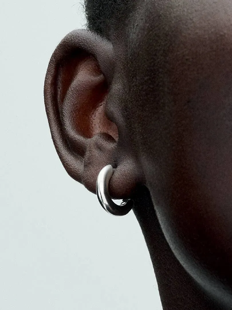 Gros plan latéral d'une boucle d'oreille créole en argent portée à l'oreille, fond neutre clair.