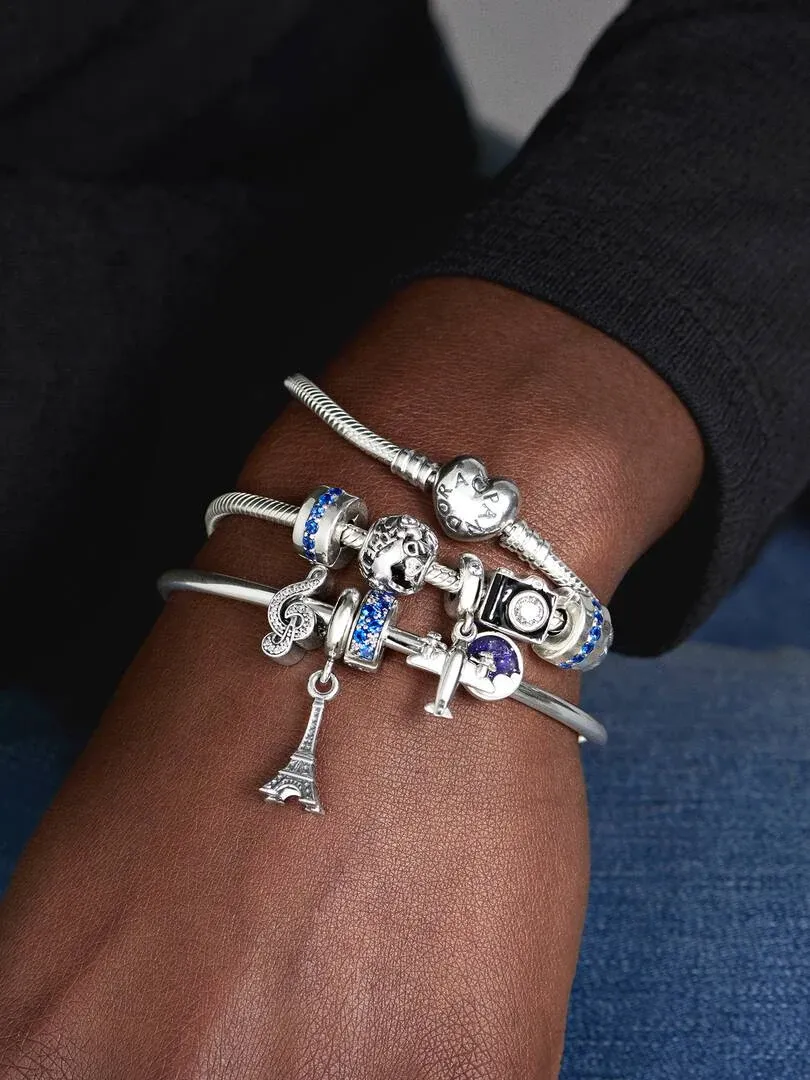 Gros plan d'un bracelet avec charms sur un poignet, focus sur le pendentif Tour Eiffel, fond flou.