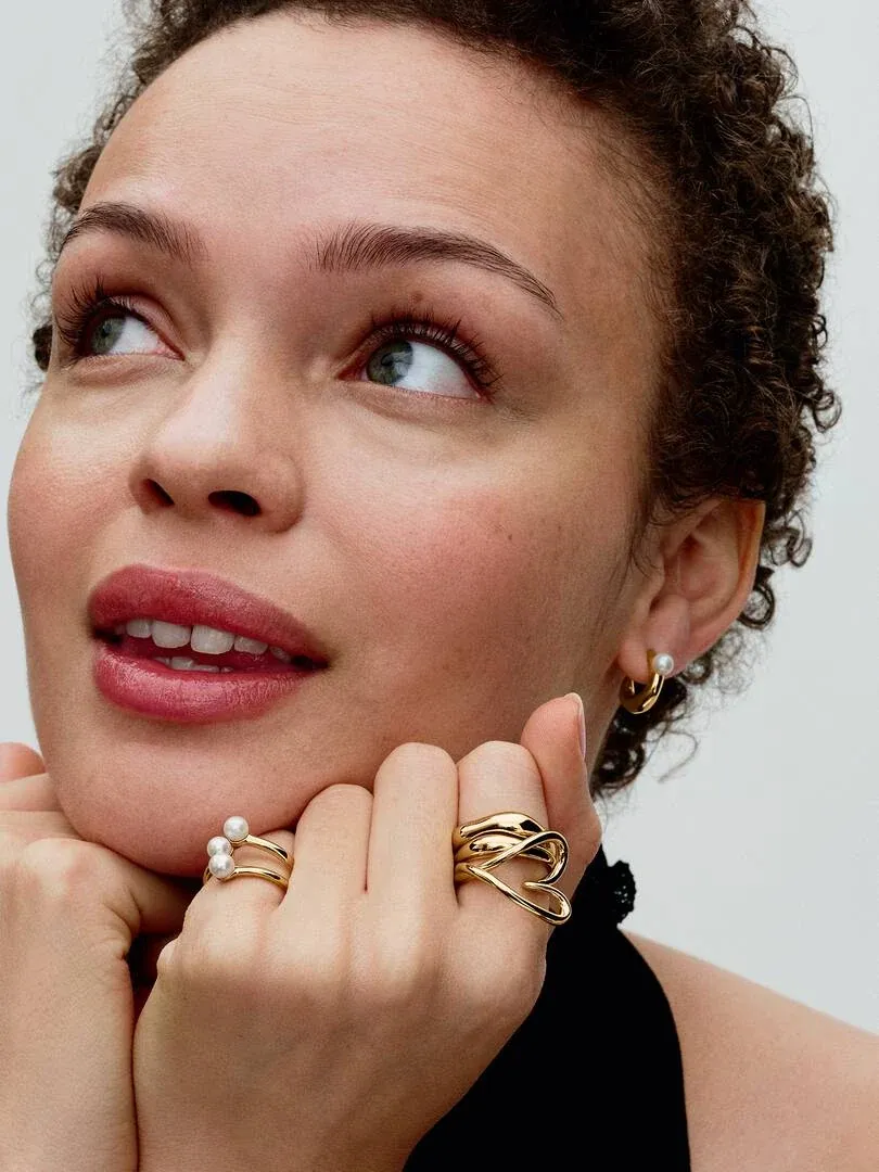 Primer plano de modelo con anillo abierto de tres bandas y perlas, junto a pendientes a juego.