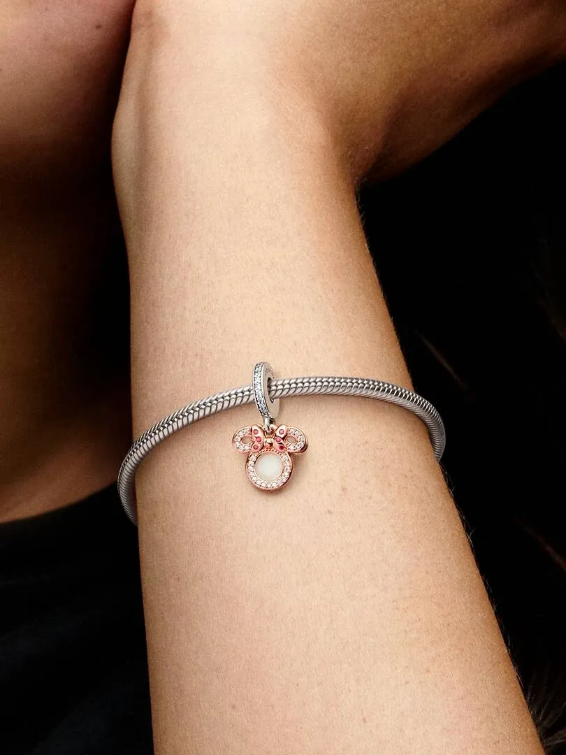 Close-up of the Minnie Mouse charm on a silver bracelet, worn on a wrist against a dark background.