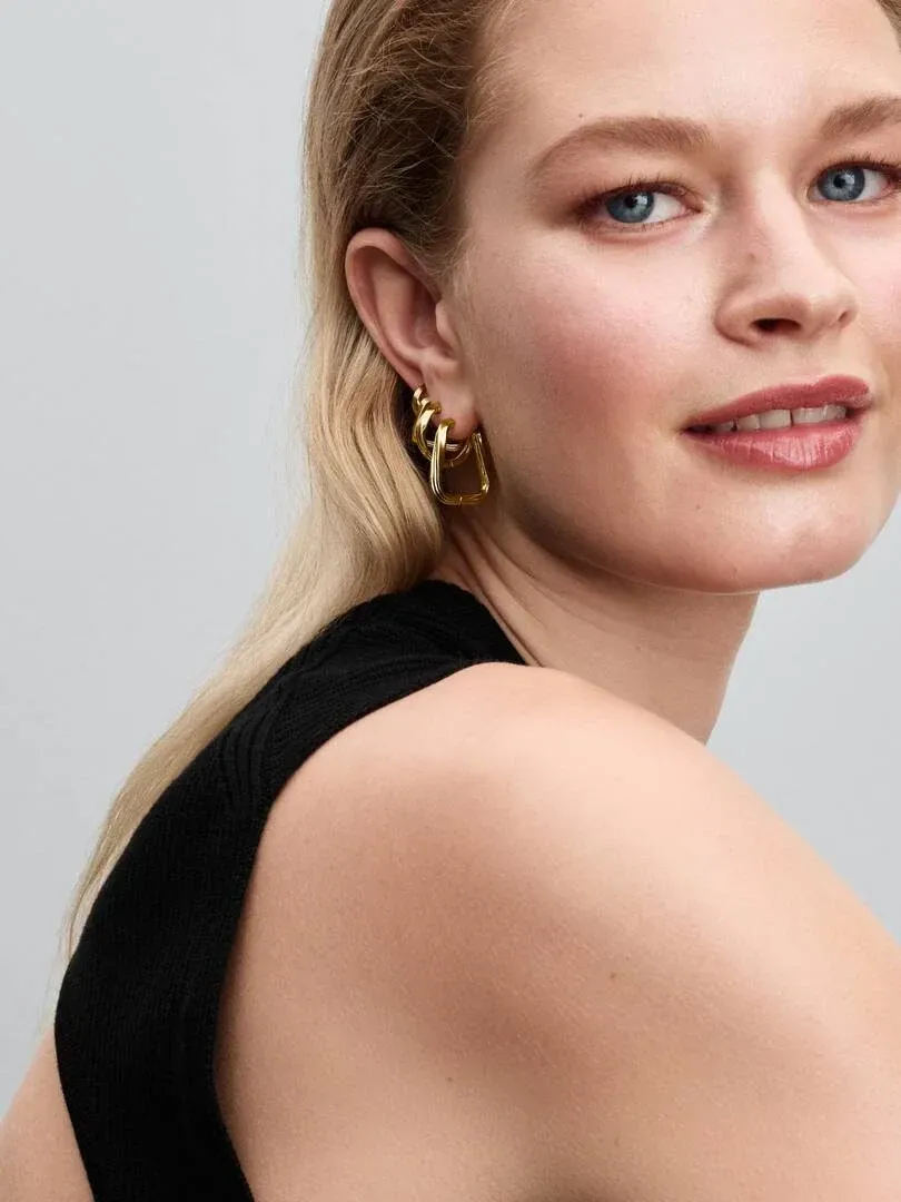Close-up of gold interlocking hoop earring worn on the ear, side view on a model.