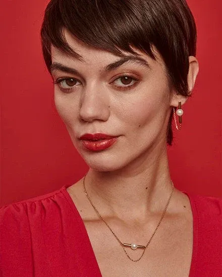 Primer plano de modelo con collar y pendientes dorados sobre fondo rojo vibrante, toma frontal.