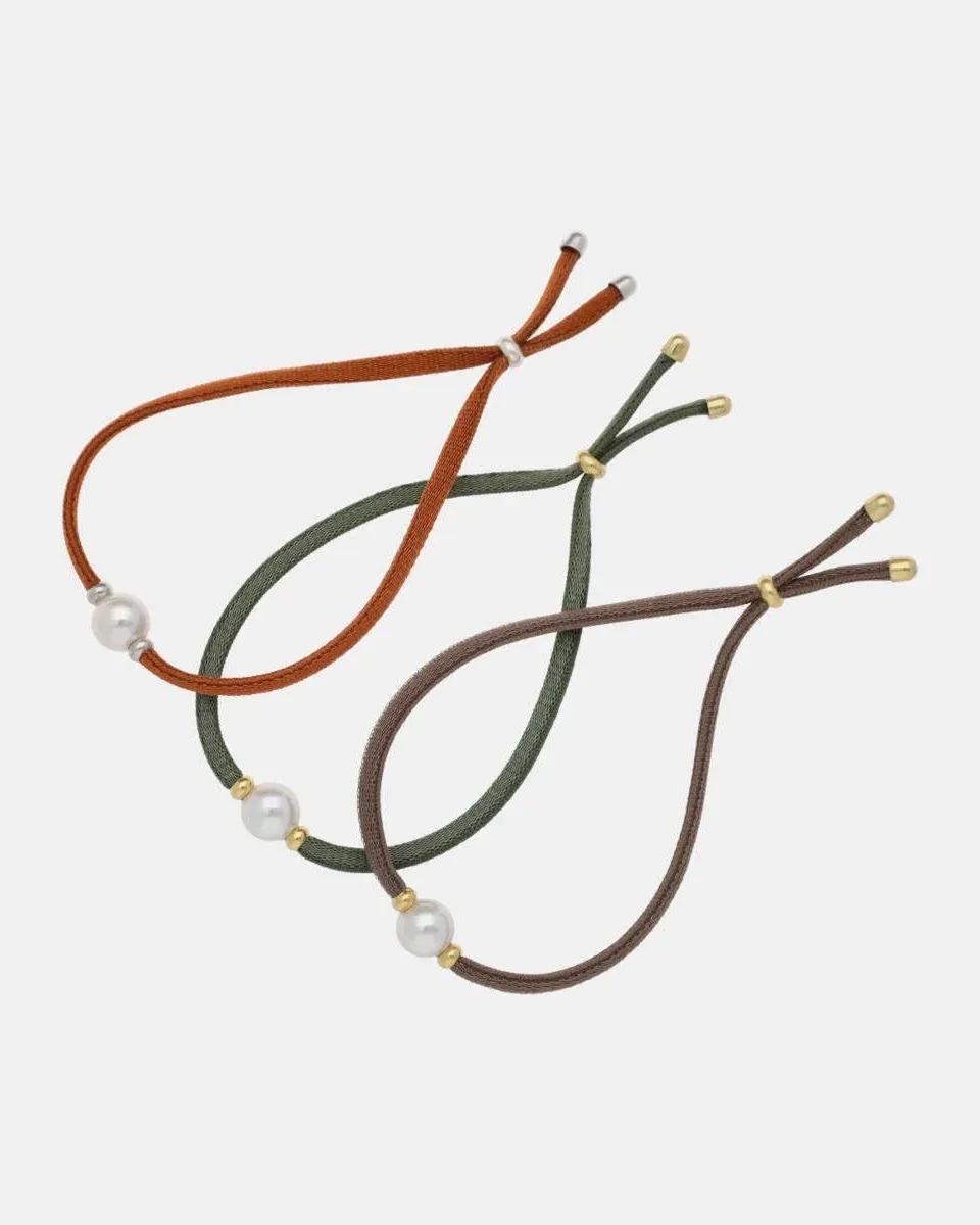 Three cord bracelets with white pearls arranged diagonally on a white background.