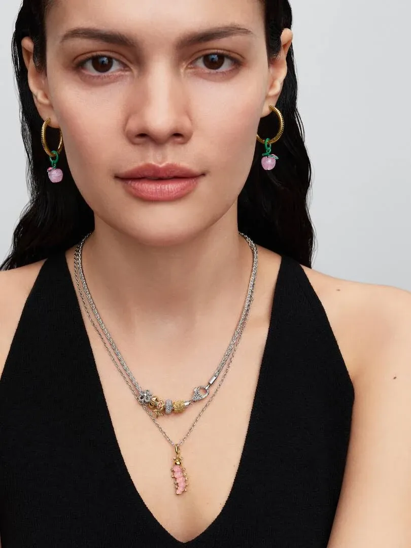 Close-up van model met oorringen en ketting met roze rups charm, neutrale achtergrond.