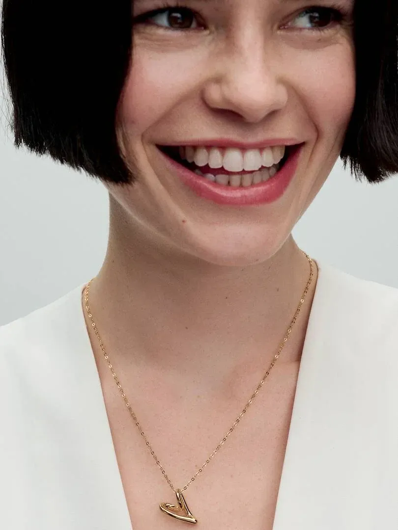 Close-up of gold heart pendant necklace on a model's neck and white blouse, front view.