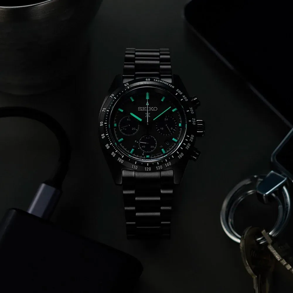 Vista cenital del reloj sobre fondo oscuro, rodeado de llaves y accesorios electrónicos.