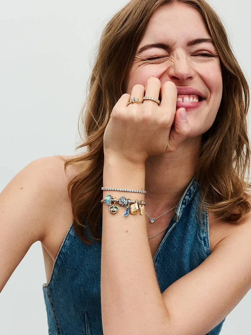 Primer plano de mano femenina con anillos y pulsera, modelo sonriendo sobre fondo blanco.