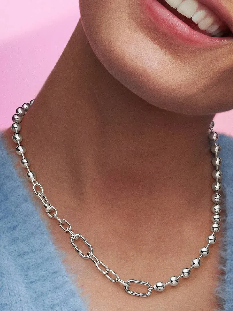 Primer plano del collar de eslabones y cuentas sobre el cuello de una modelo, fondo rosa suave.