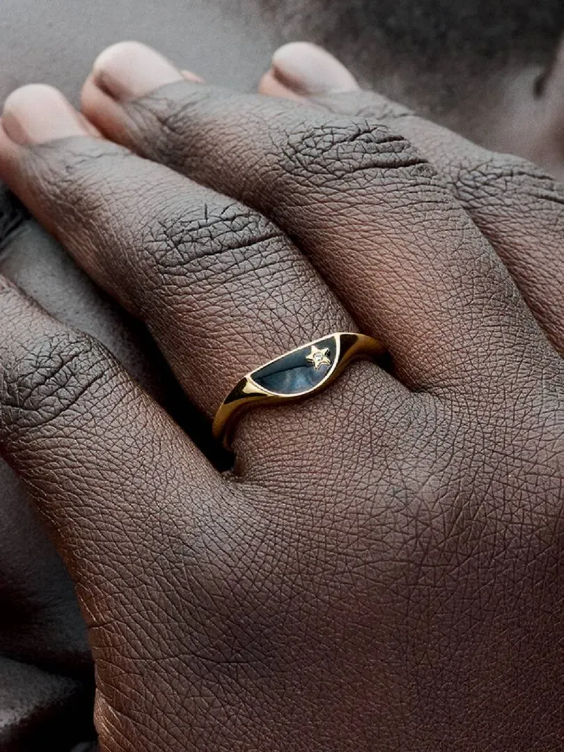 Primer plano del anillo con esmalte negro y estrella, puesto en un dedo sobre fondo desenfocado.