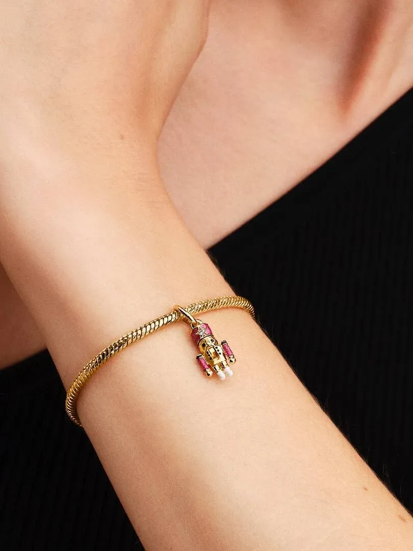 Gros plan du charm casse-noisette sur un bracelet doré, porté au poignet sur fond noir.