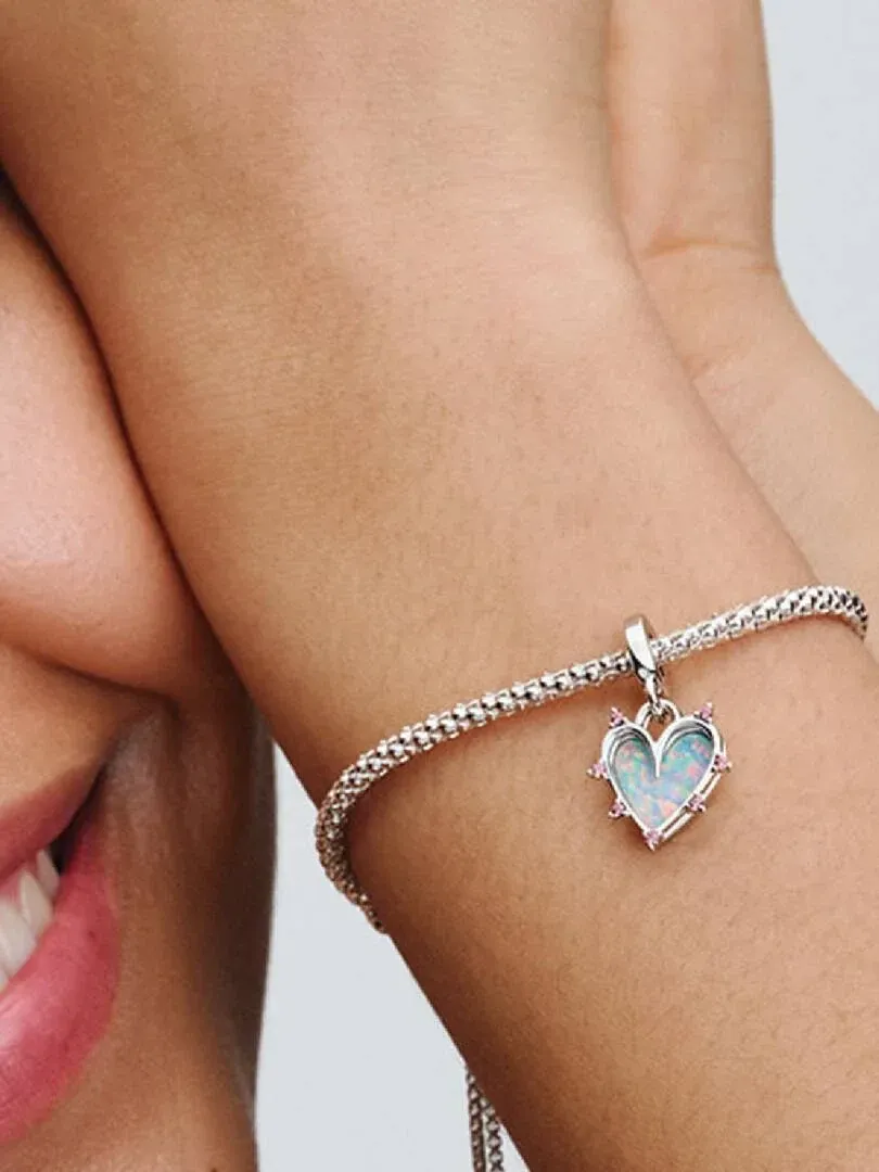 Close-up of pink heart charm on a silver bracelet, worn on a model's wrist.