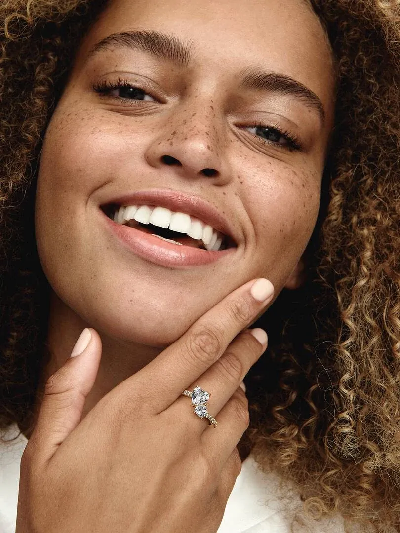 Primer plano de la mano en el rostro, mostrando el anillo con corazones y circonitas sobre piel.