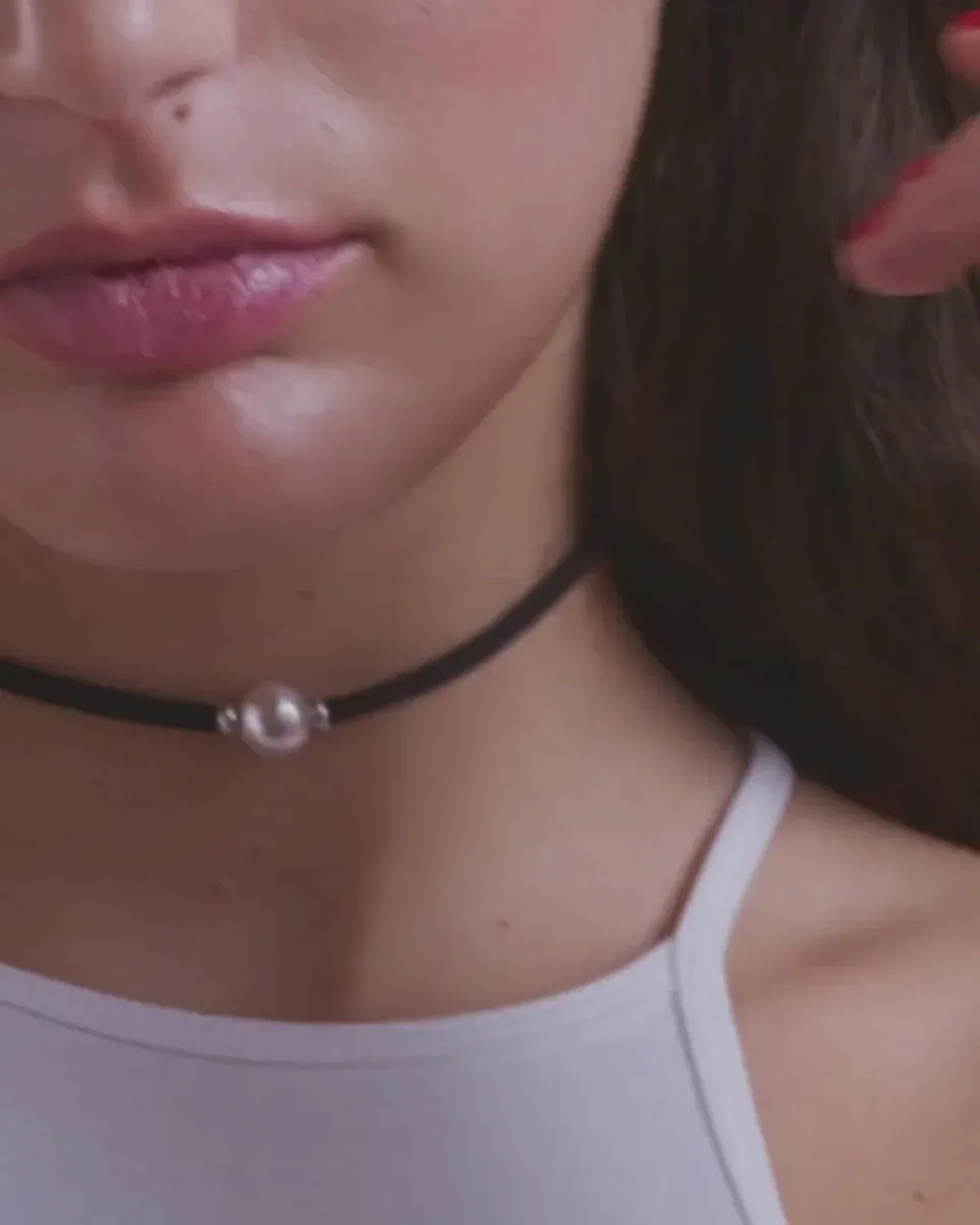 Gros plan du collier noir avec perle blanche porté au cou, vue de profil.