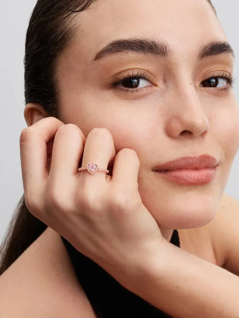 Gros plan de la bague cœur rose au doigt de la modèle, posé contre sa joue.